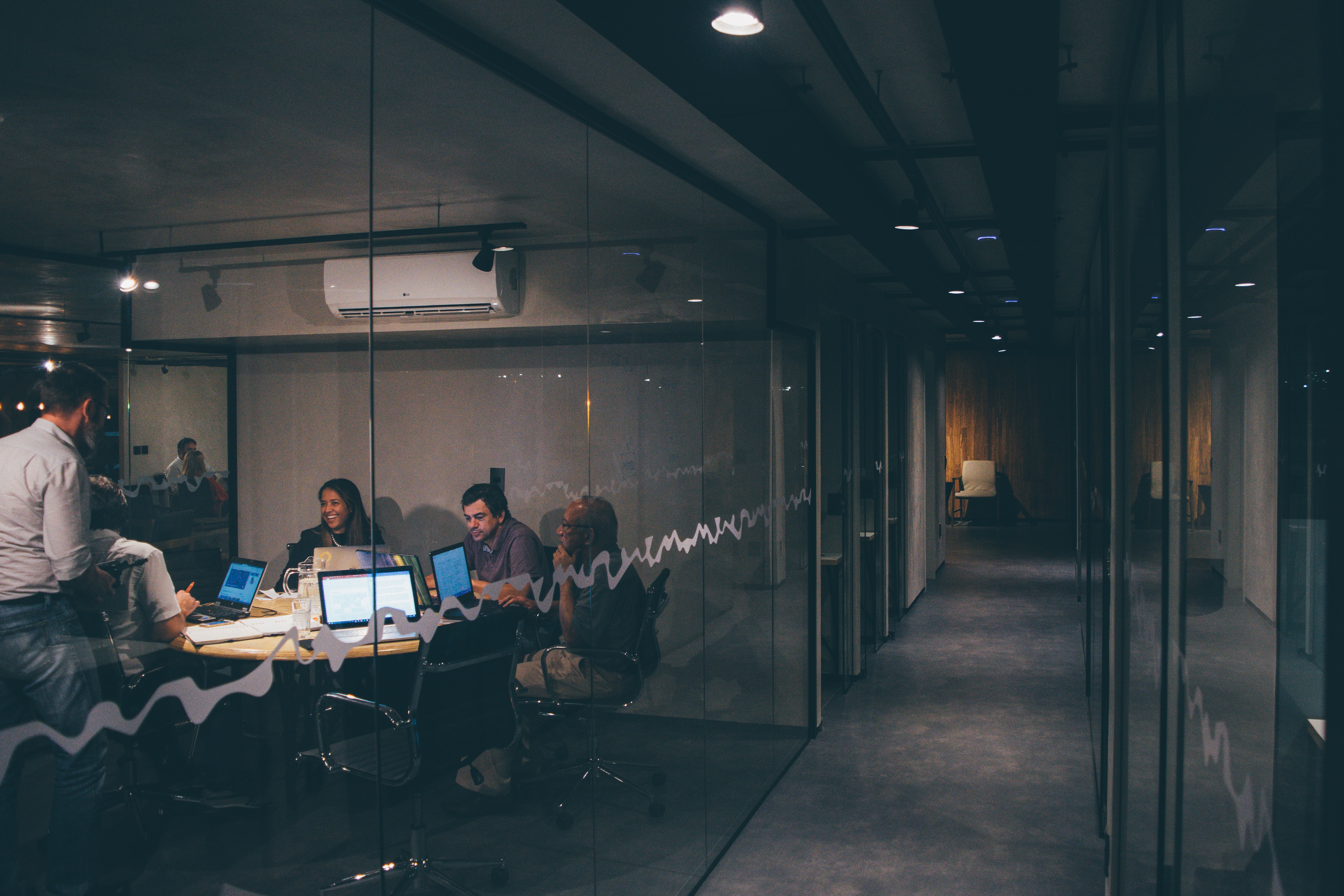 Dimly lit office space hallway with a conference room to the left side where a team of people are collaborating