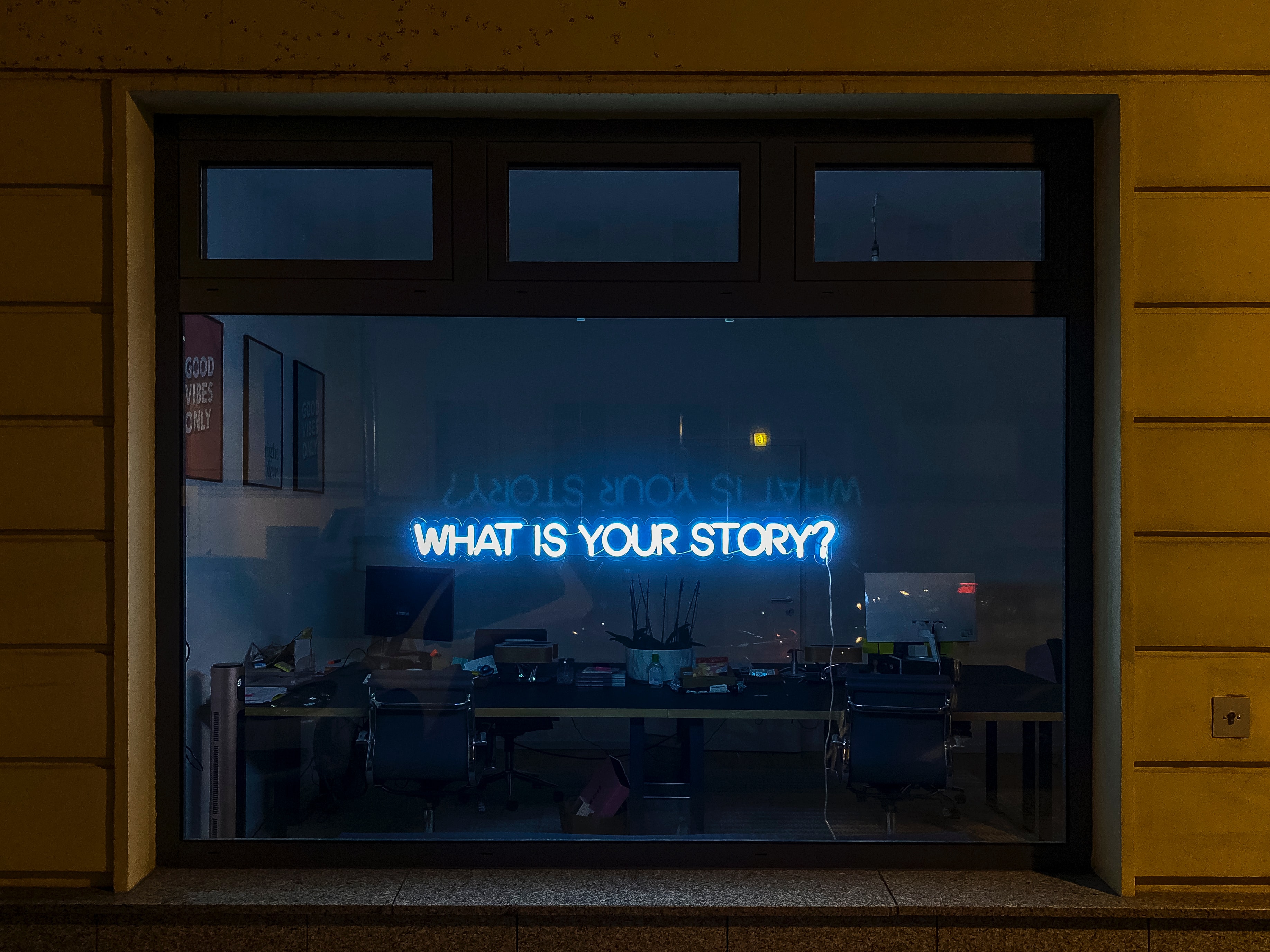 Office window with a neon sign that displays the question, what is your story?